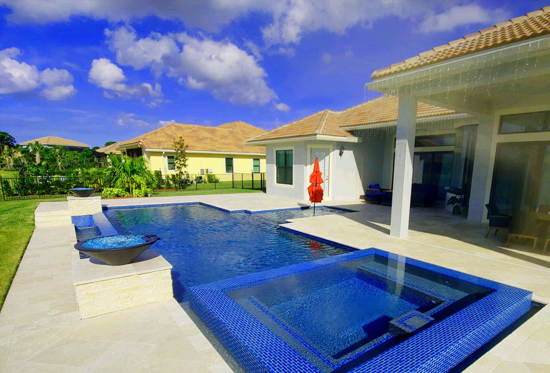Backyard pool with blue mosaic tile, a white house, and a sunny sky.