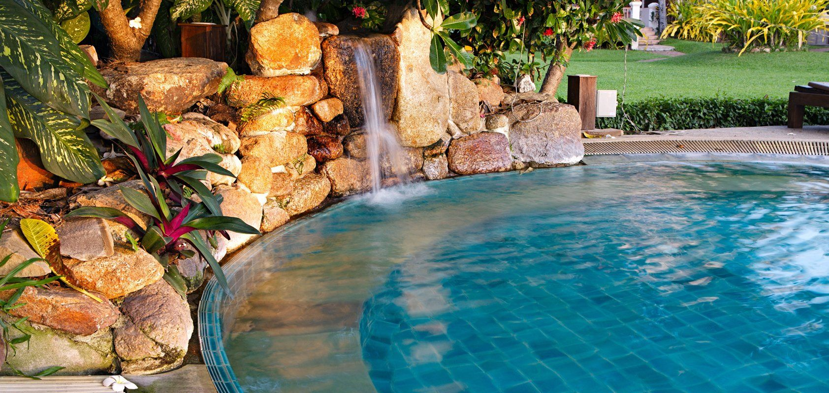 Pool with waterfall feature and lush greenery.