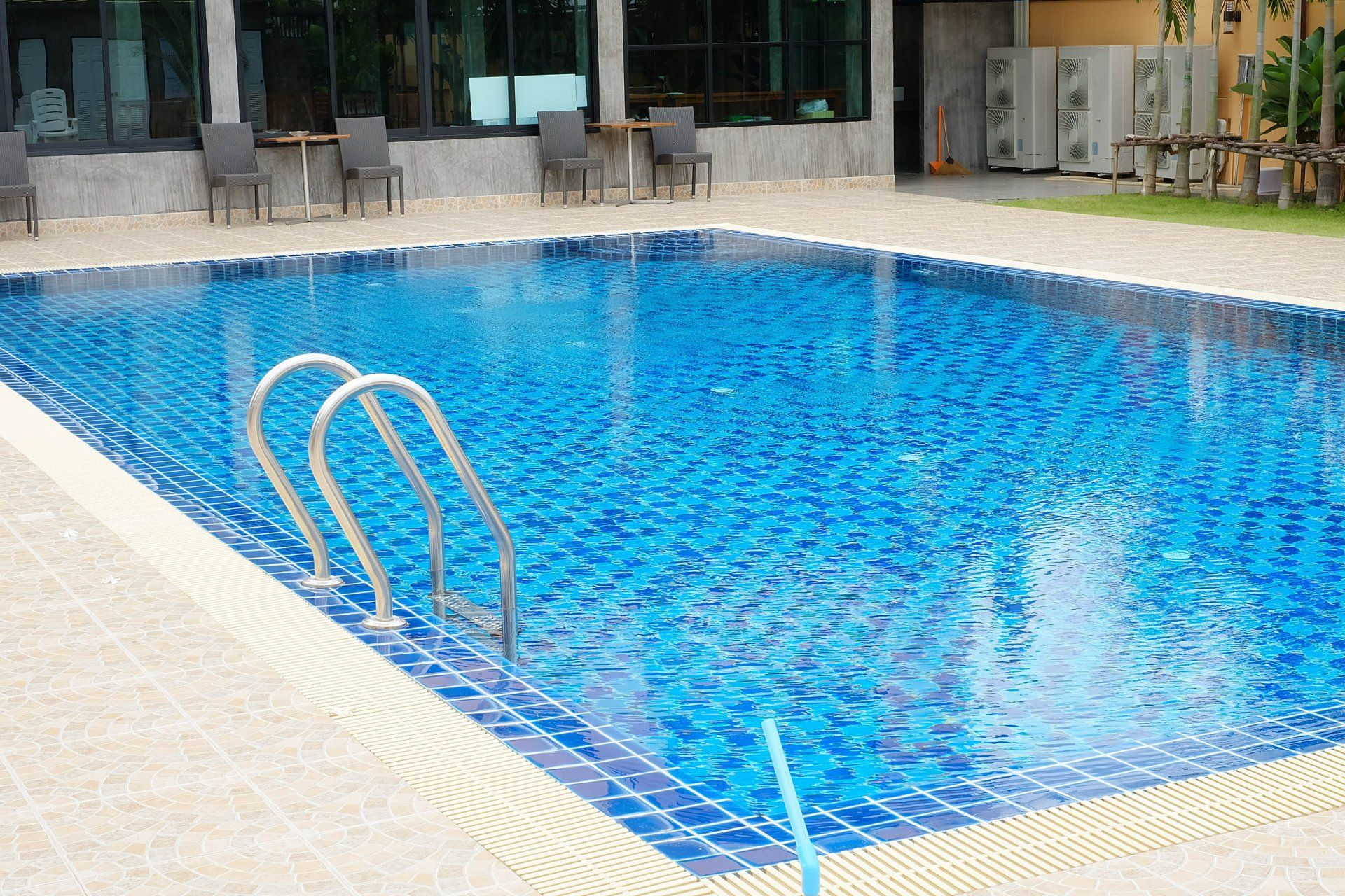 Swimming pool with blue tiles, stainless steel ladder, and building in the background.