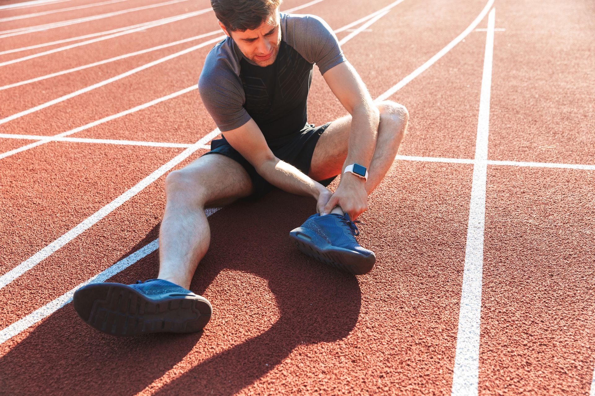 Tired sportsman suffering from ankle pain in an outdoors running field.