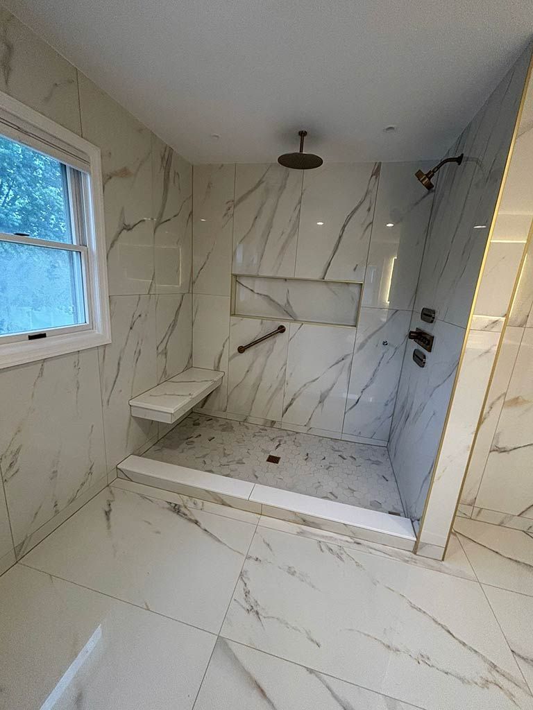 Modern tiled bathroom with a walk-in shower, bench, window, and overhead light