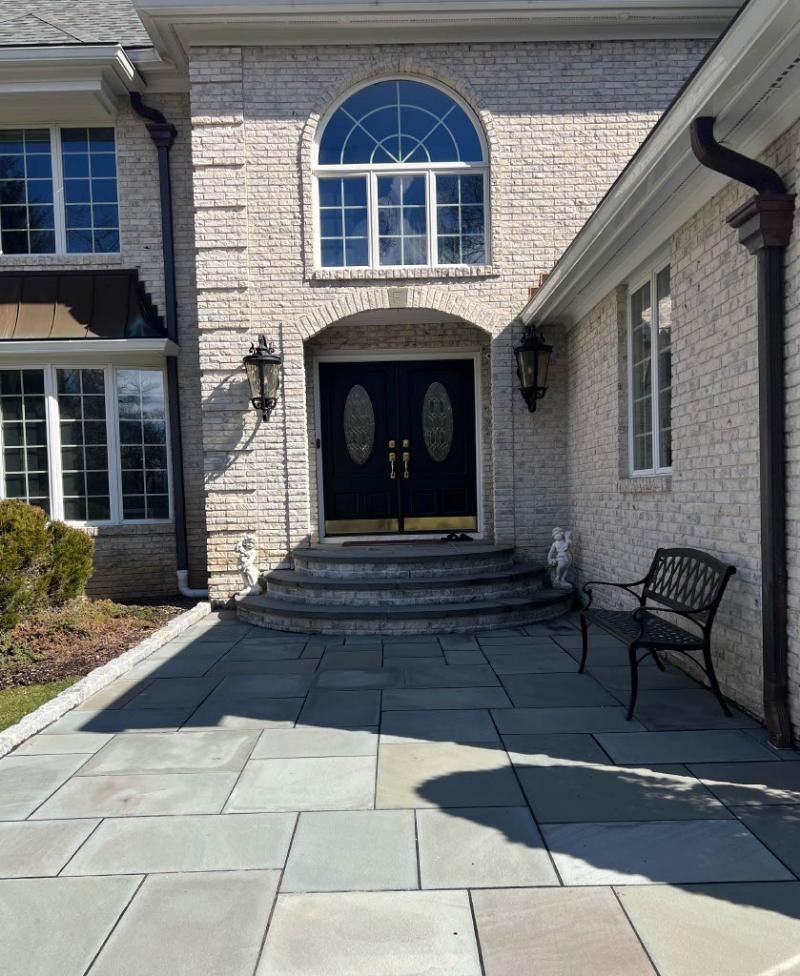 Front entry of a stone house with double doors, arched window, and a bench along the walkway