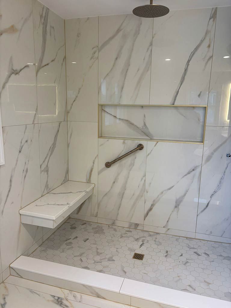 Modern tiled shower with bench, wall niche, and handheld showerhead in white marble-look finish