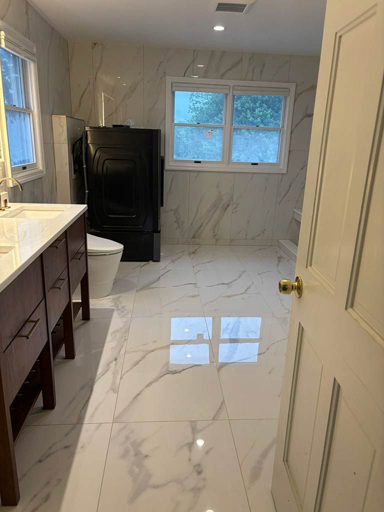 Modern bathroom with marble tile, vanity, toilet, black cabinet, and window.