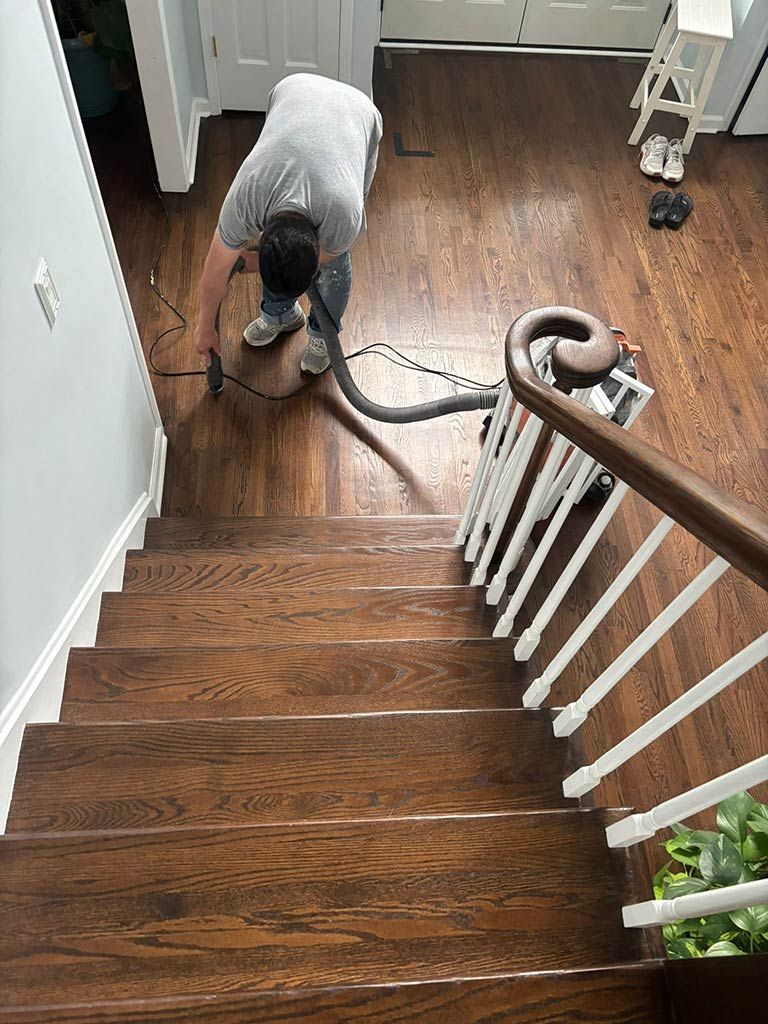 Person vacuuming a wooden staircase with a canister vacuum and hose.