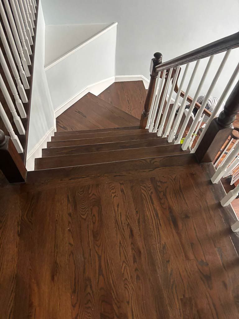 Wooden staircase landing with white walls and dark railings, viewed from the top.