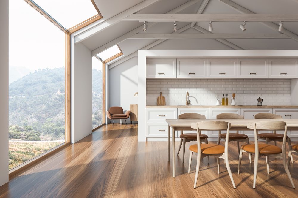 Modern loft kitchen and dining area with wood floors, white cabinets, and large windows overlooking mountains
