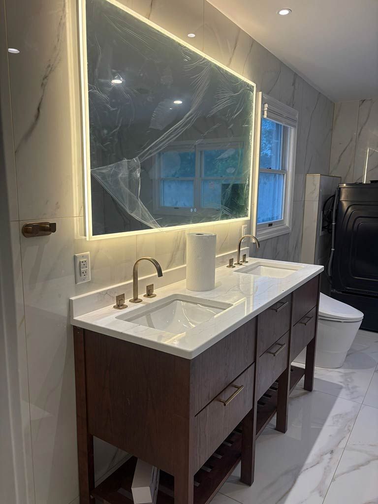 Modern bathroom with double vanity, illuminated mirror, marble floor, and window wrapped in plastic sheeting.