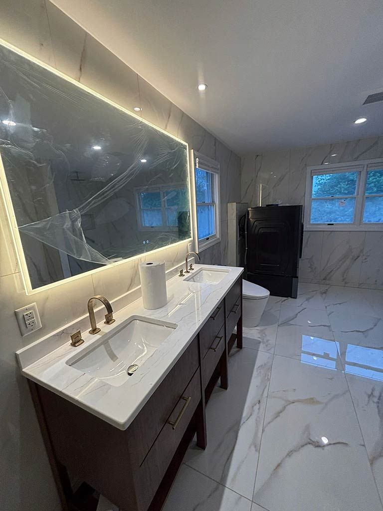 Modern bathroom with marble floors, dark vanity, lit mirror, and a window with blinds