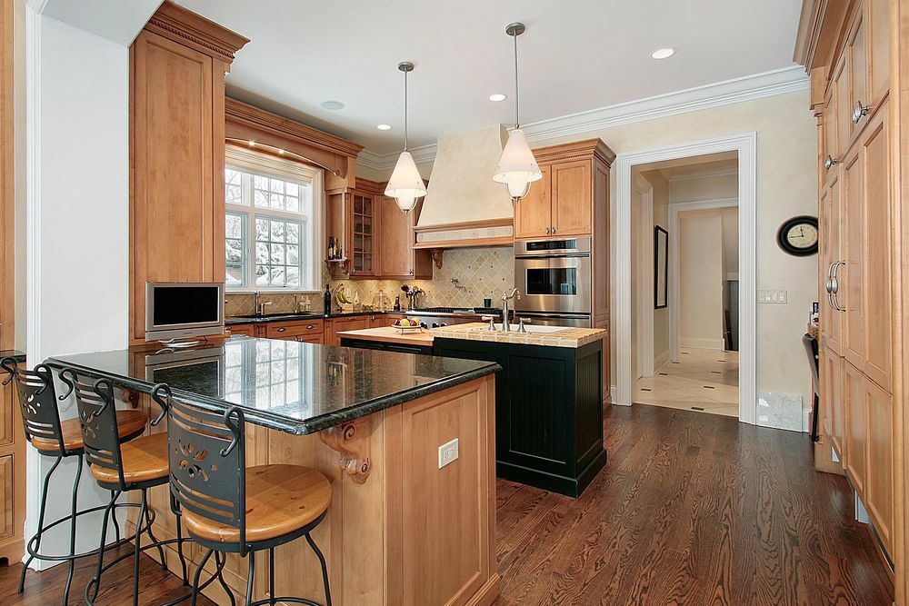 Spacious kitchen with wood cabinets, granite island, pendant lights, and hardwood floors.