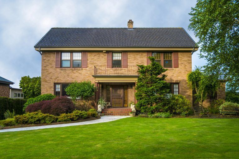 Two-story brick house with a manicured lawn and trees in front