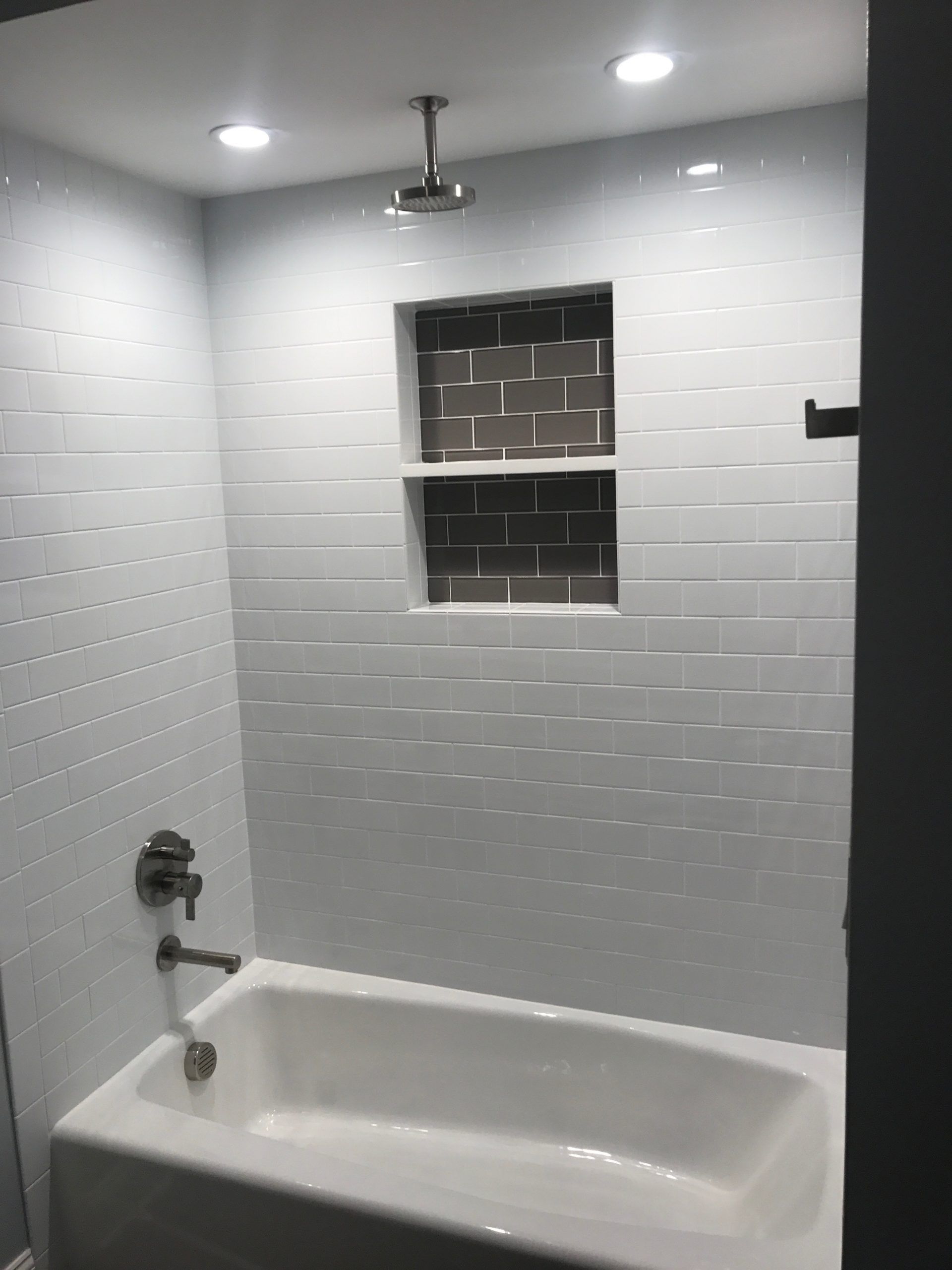 Small bathroom with white subway tiles, a bathtub, and a tiled shower niche under ceiling lights.