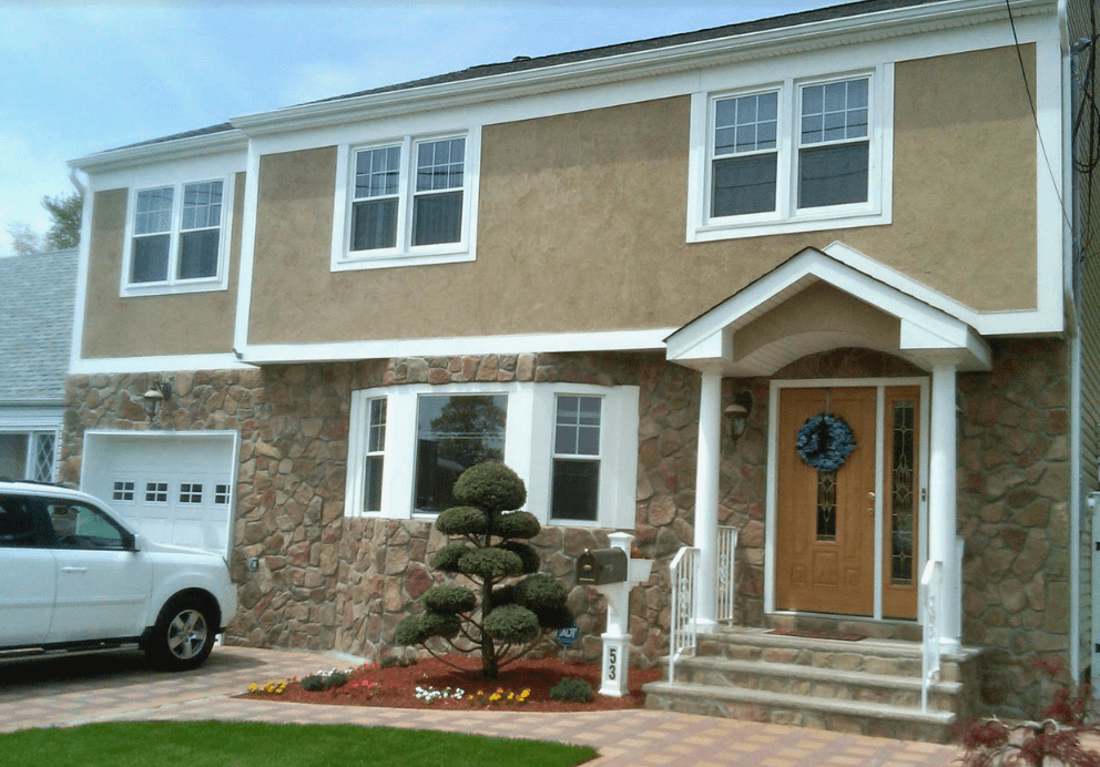 Two-story beige house with white trim, stone accents, and a front porch beside a garage.