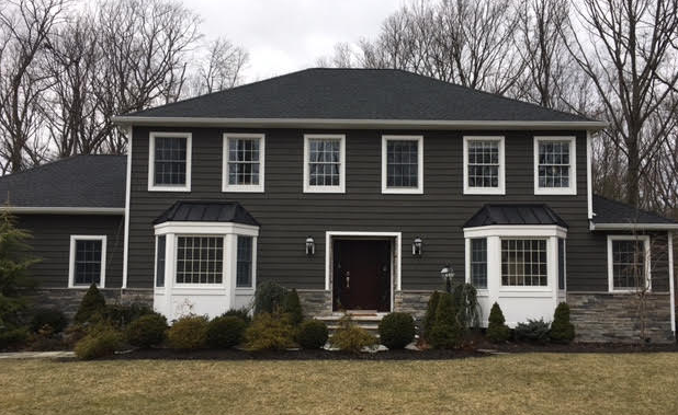 Two-story dark gray house with white trim and bay windows, fronted by shrubs and leafless trees