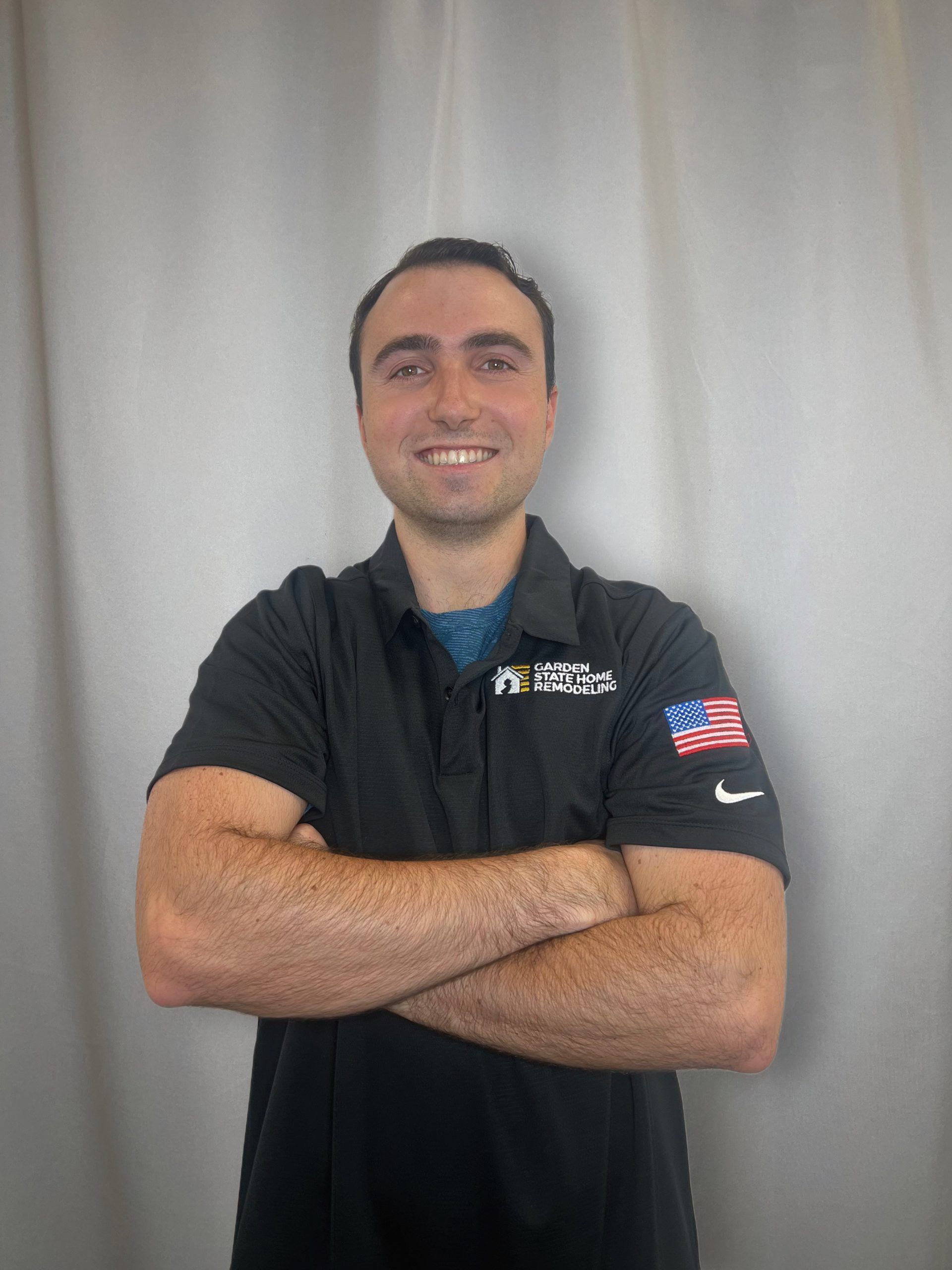 Smiling person in a black polo shirt with arms crossed against a light gray backdrop