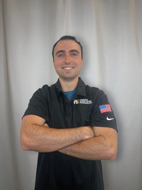 Smiling person in a black polo shirt with arms crossed against a light gray backdrop