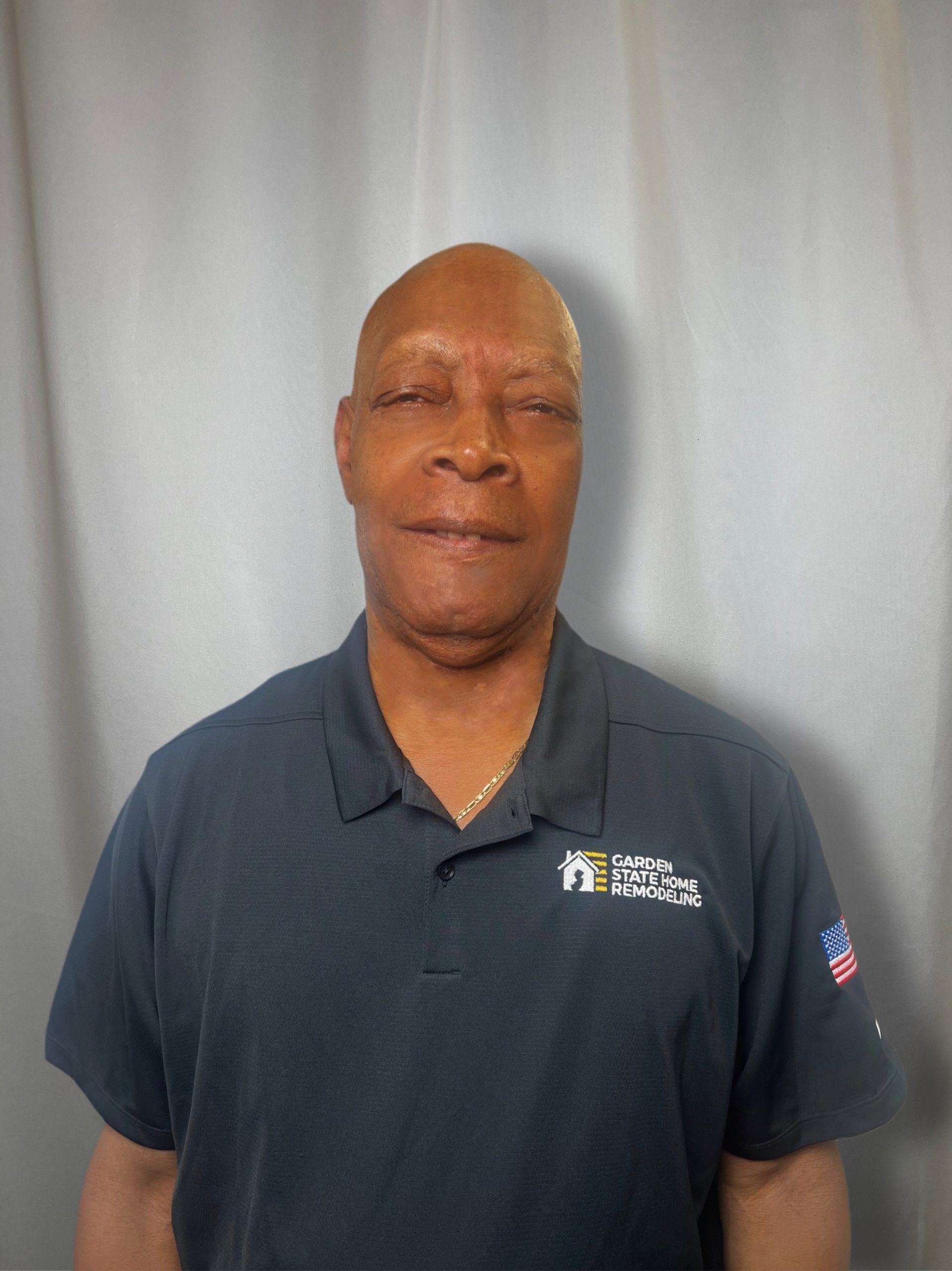 Man standing against a gray curtain, wearing a dark navy polo shirt.