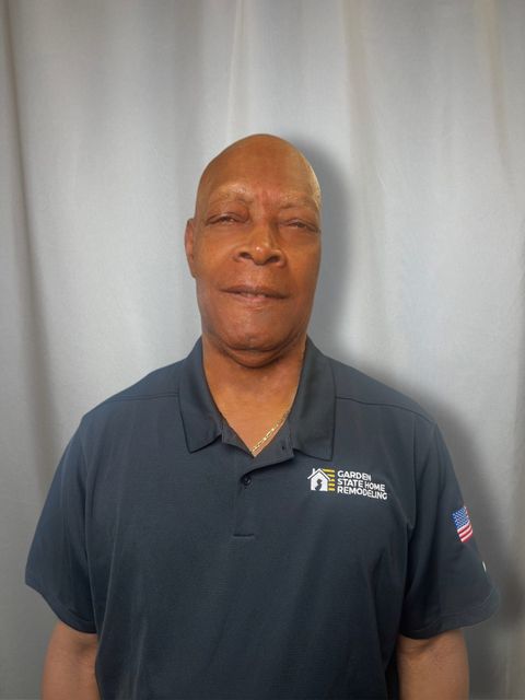 Man standing against a gray curtain, wearing a dark navy polo shirt.
