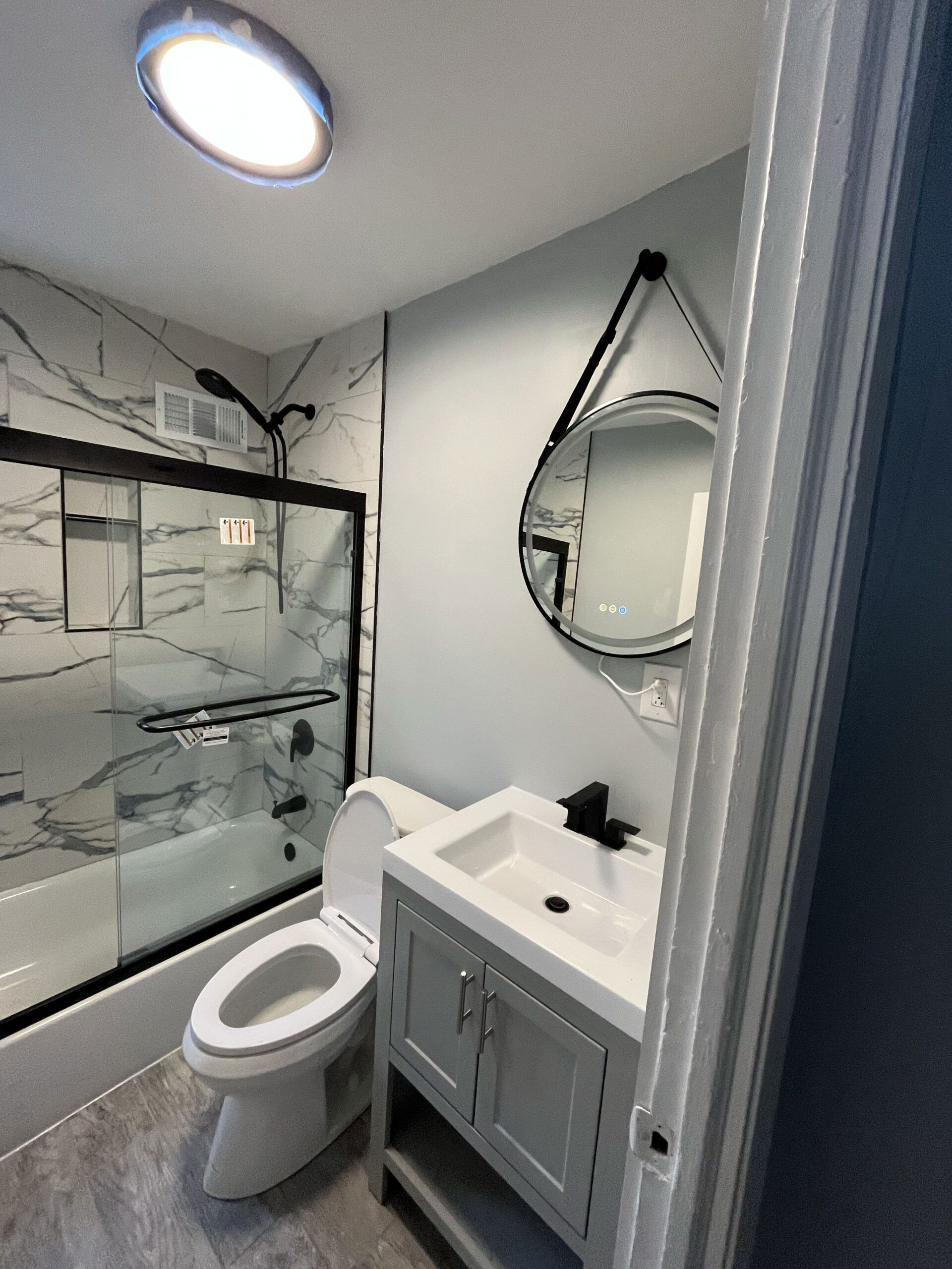 Modern bathroom with glass shower, toilet, gray vanity, and round mirror