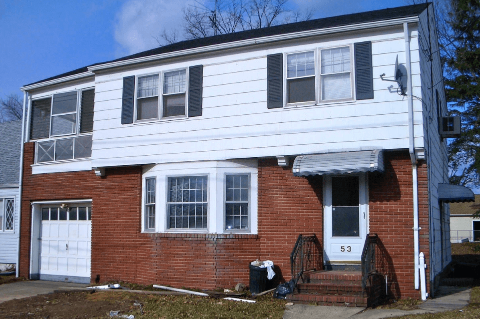 Two-story house with white siding, red brick, and a front porch in a residential neighborhood.