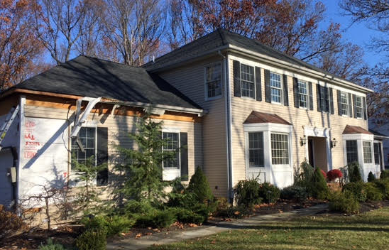Two-story beige house with white trim, dark roof, and a small front garden under leafless trees