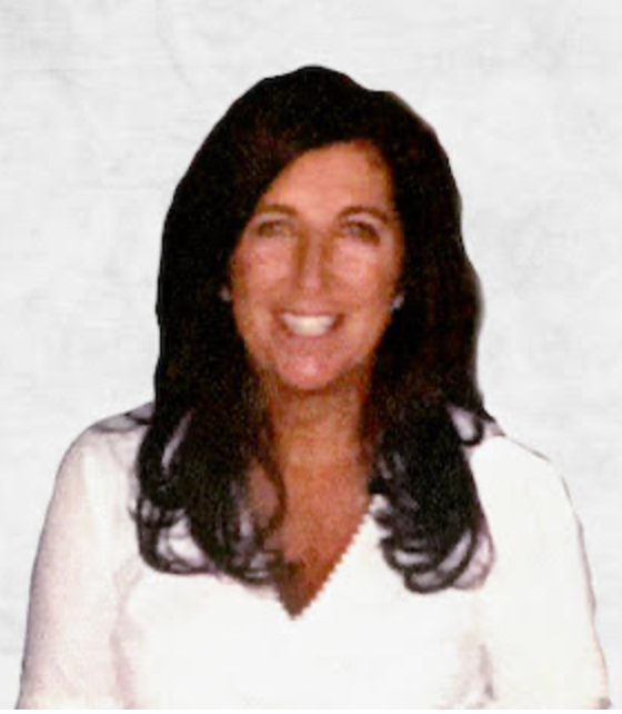 Smiling woman with long dark hair wearing a white top against a light background