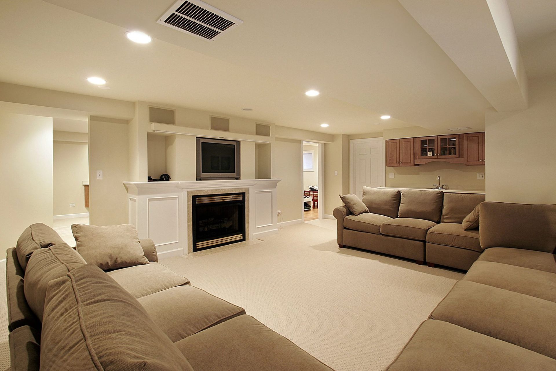Finished basement living room with beige sofas, carpet, fireplace, and TV.