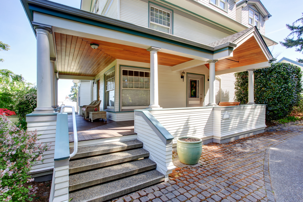 Front porch of a white house with wooden steps, columns, and a covered patio.