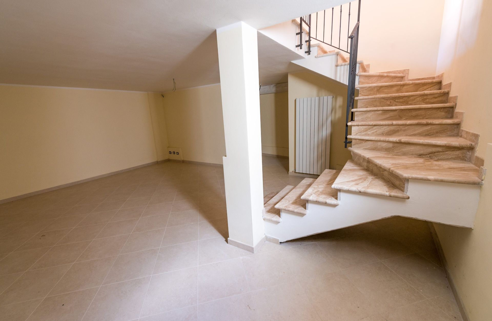 Empty beige room with carpeted stairs and a landing on the right.
