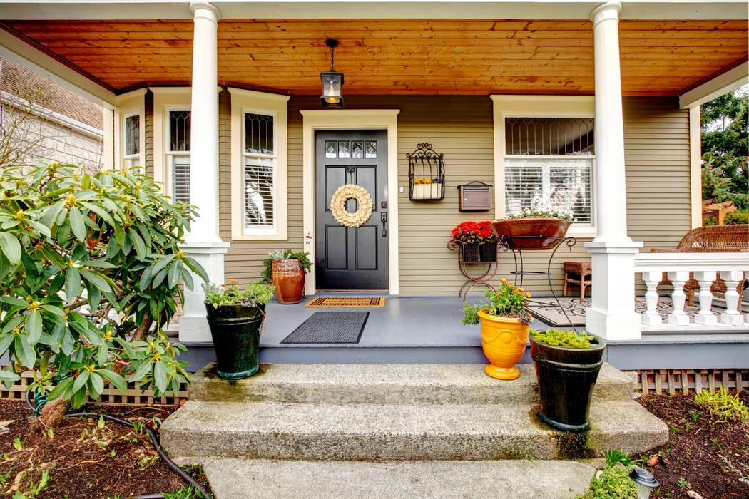 Front porch of a house with gray door, white columns, potted plants, and stone steps