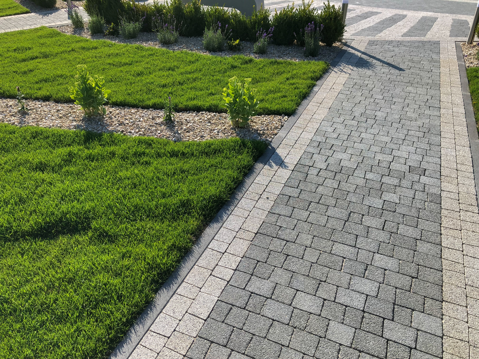 Stone walkway beside neatly trimmed green grass and hedges in a landscaped garden.