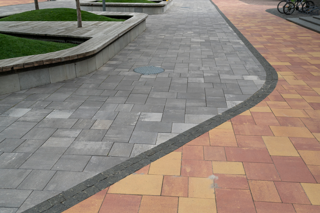 Curved gray and yellow brick walkway beside landscaped planters and a bicycle in the distance