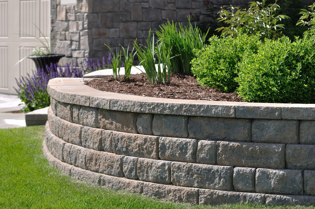 Curved stone retaining wall with green shrubs and grass in a landscaped yard
