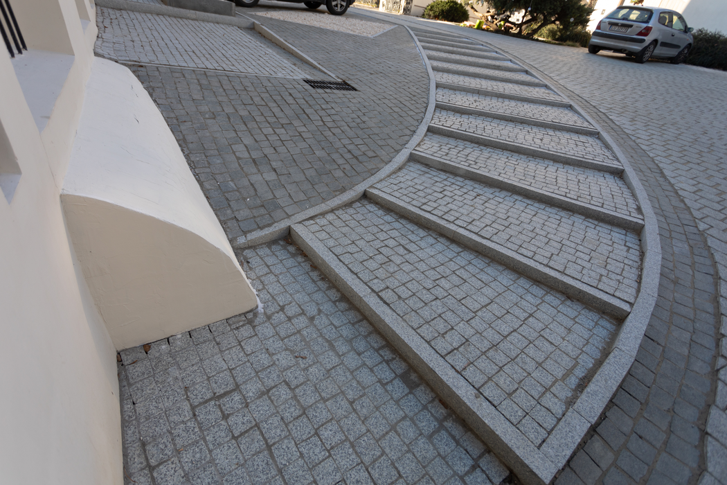 Curved tiled outdoor steps beside a white wall, leading up a sloped driveway with parked cars.