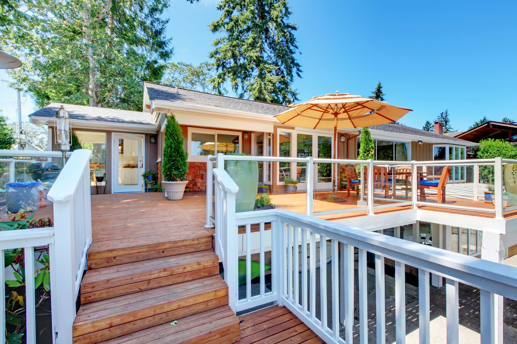 Front porch with white railing, wooden steps, and a patio umbrella on a sunny house deck