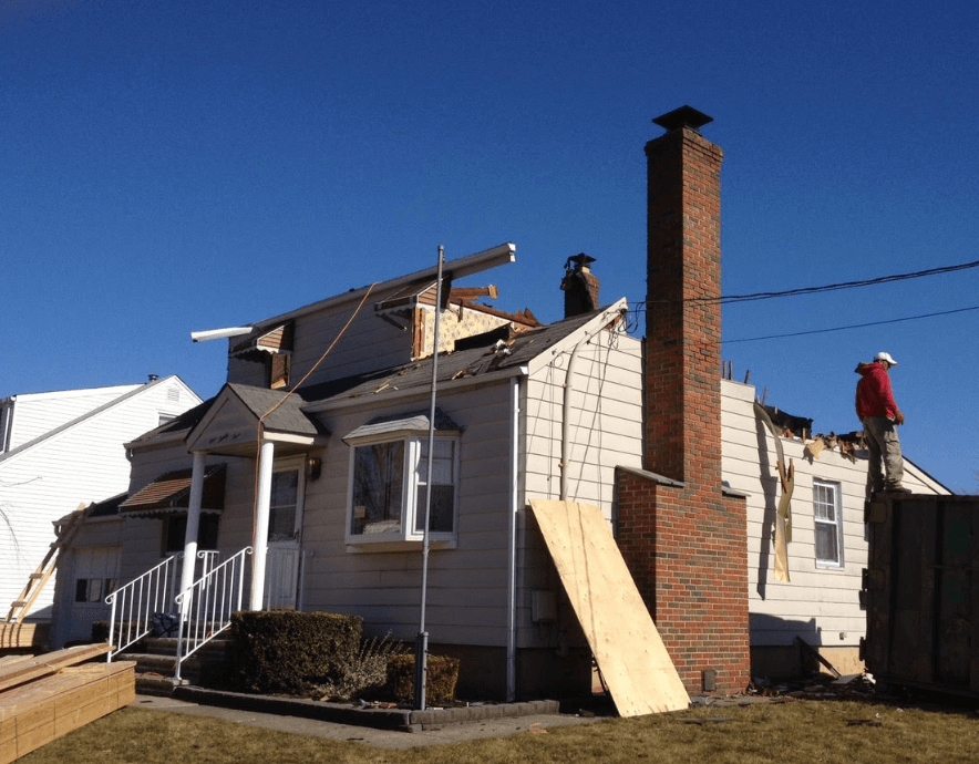 House roof under repair with workers, wooden boards, and a tall brick chimney on a sunny day