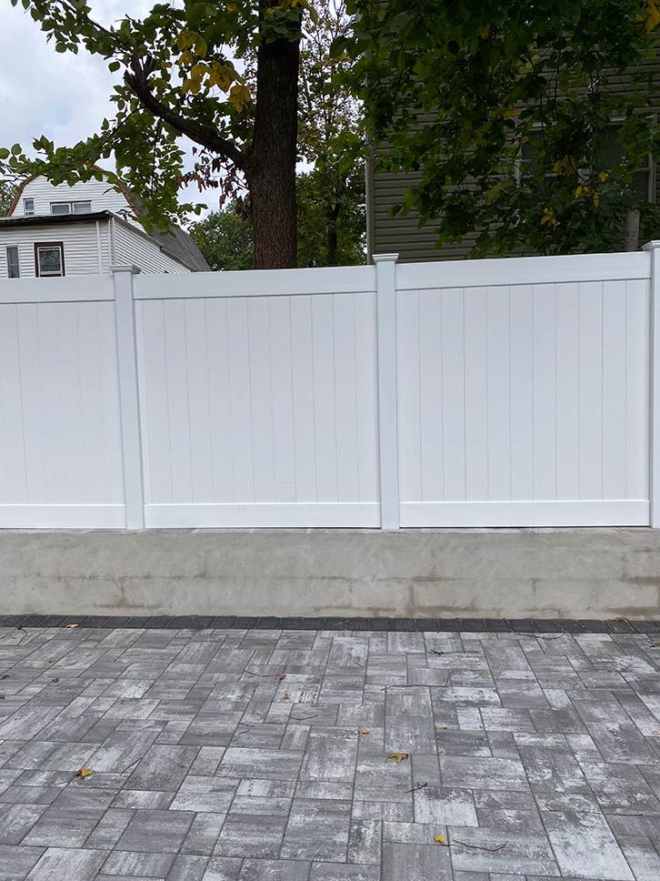 White vinyl fence along a cobblestone street with trees behind it