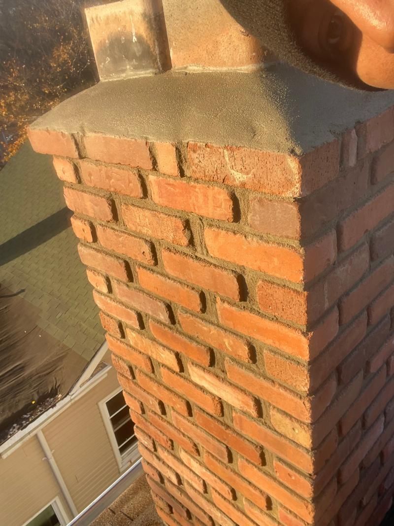 Brick chimney with a concrete cap, viewed close up in warm sunlight.