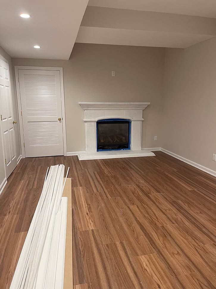 Empty living room with wood floor, white fireplace, and recessed ceiling lights.