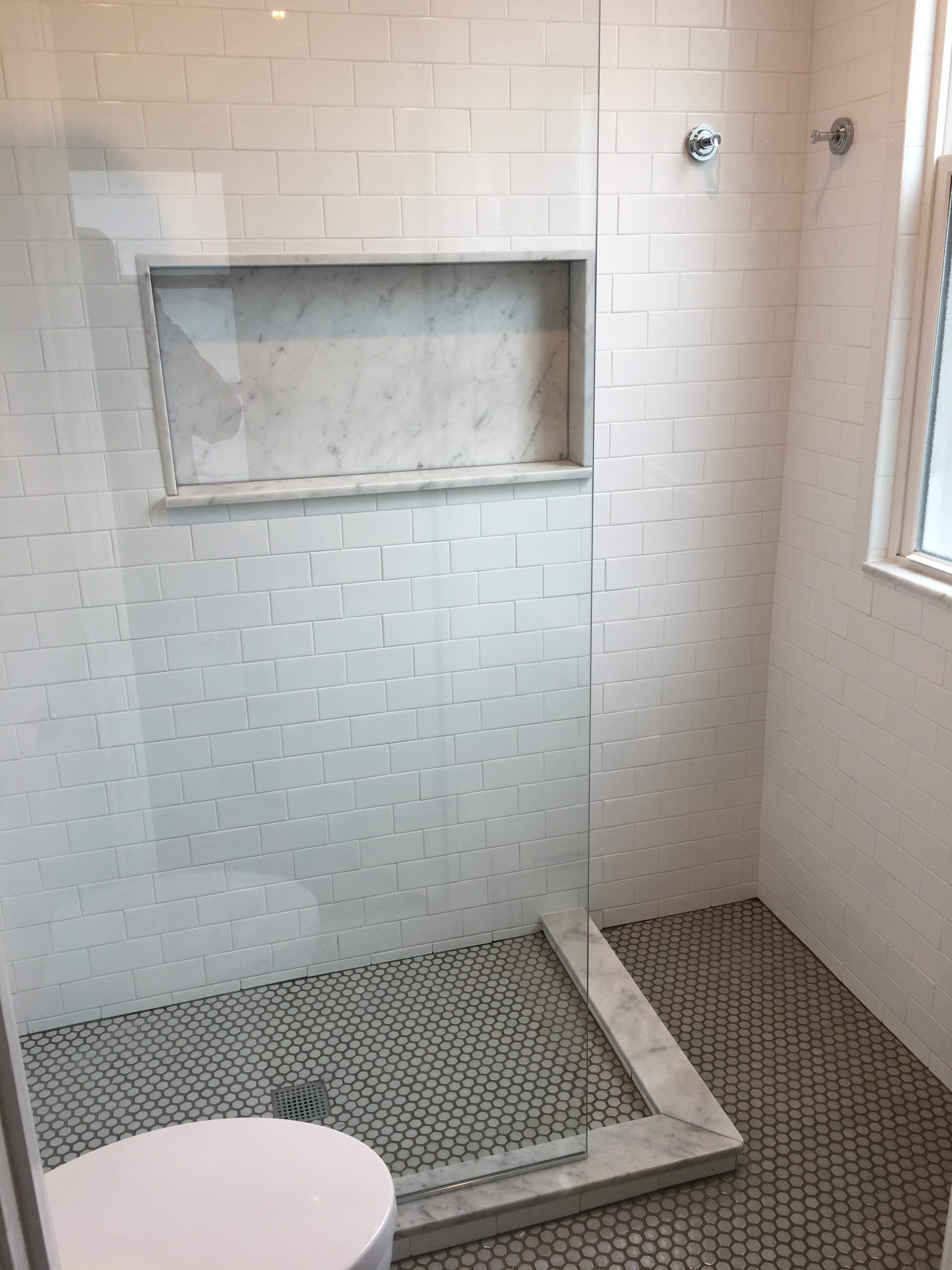 White-tiled walk-in shower with mosaic floor, built-in niche, and window light