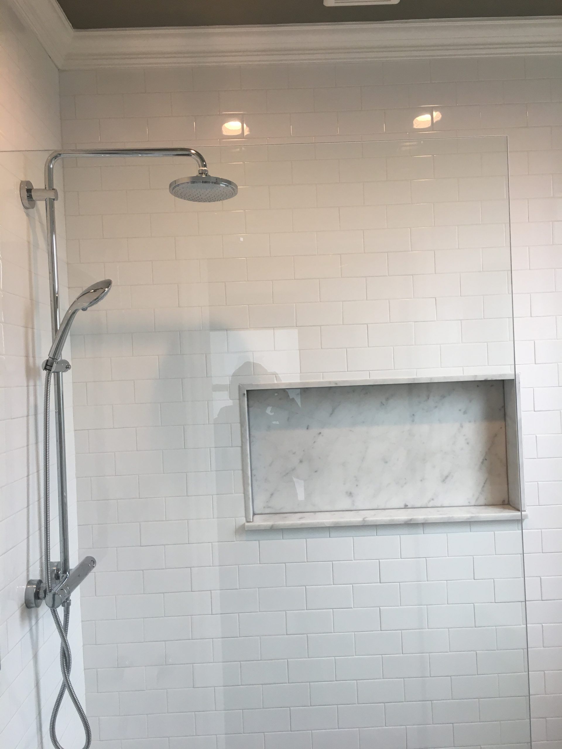 White-tiled shower stall with a rainfall showerhead, handheld sprayer, and recessed wall niche.