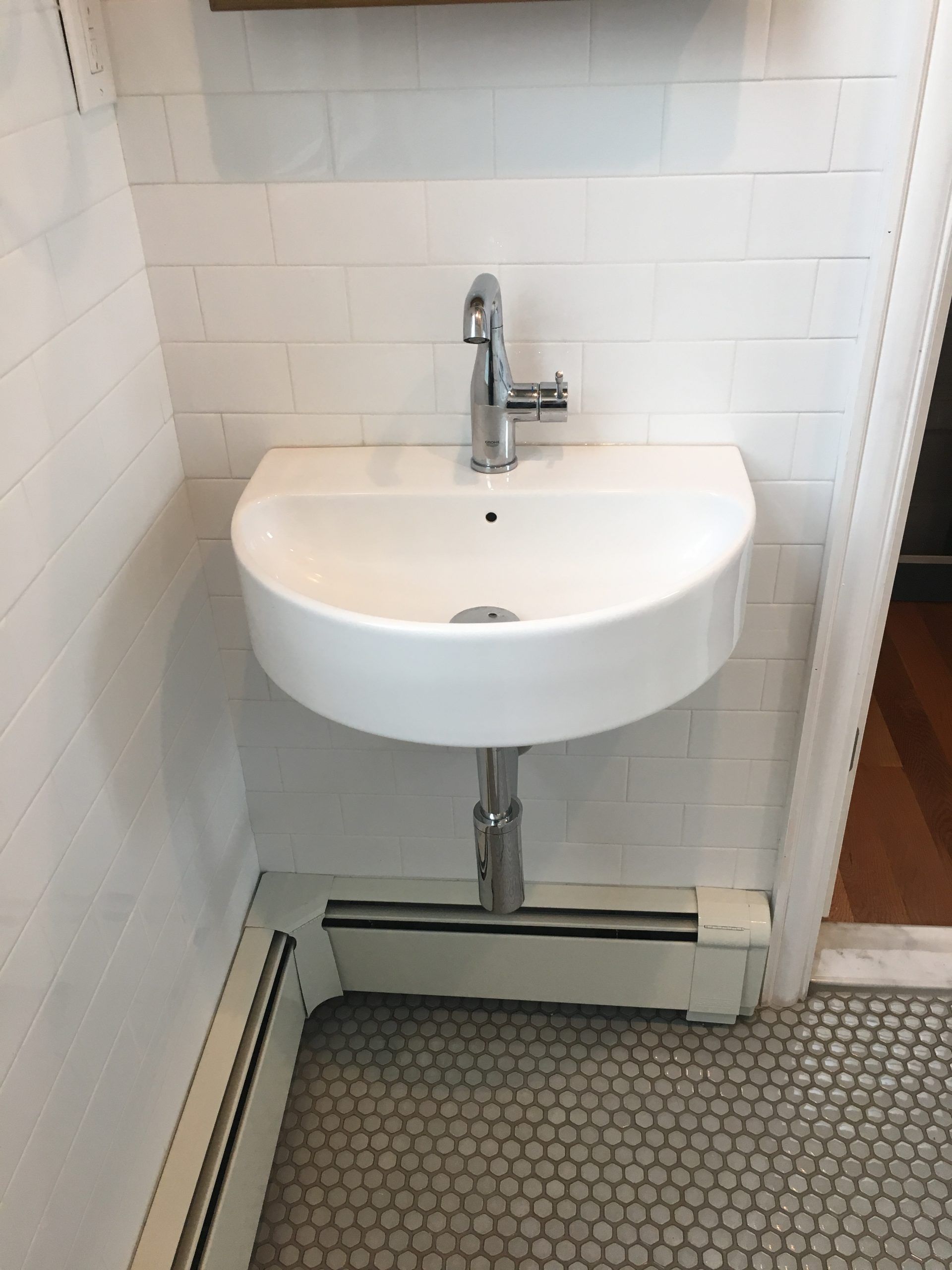 Compact white wall-mounted sink in a small tiled bathroom alcove