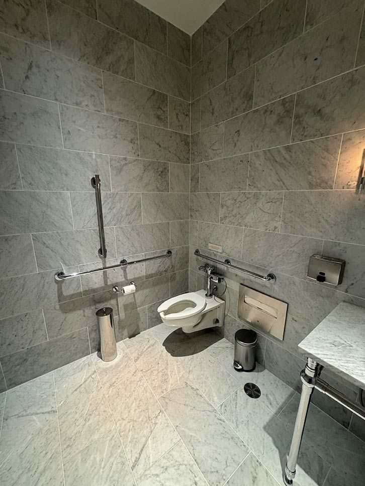 Accessible restroom with a toilet, grab bars, and gray tiled walls and floor