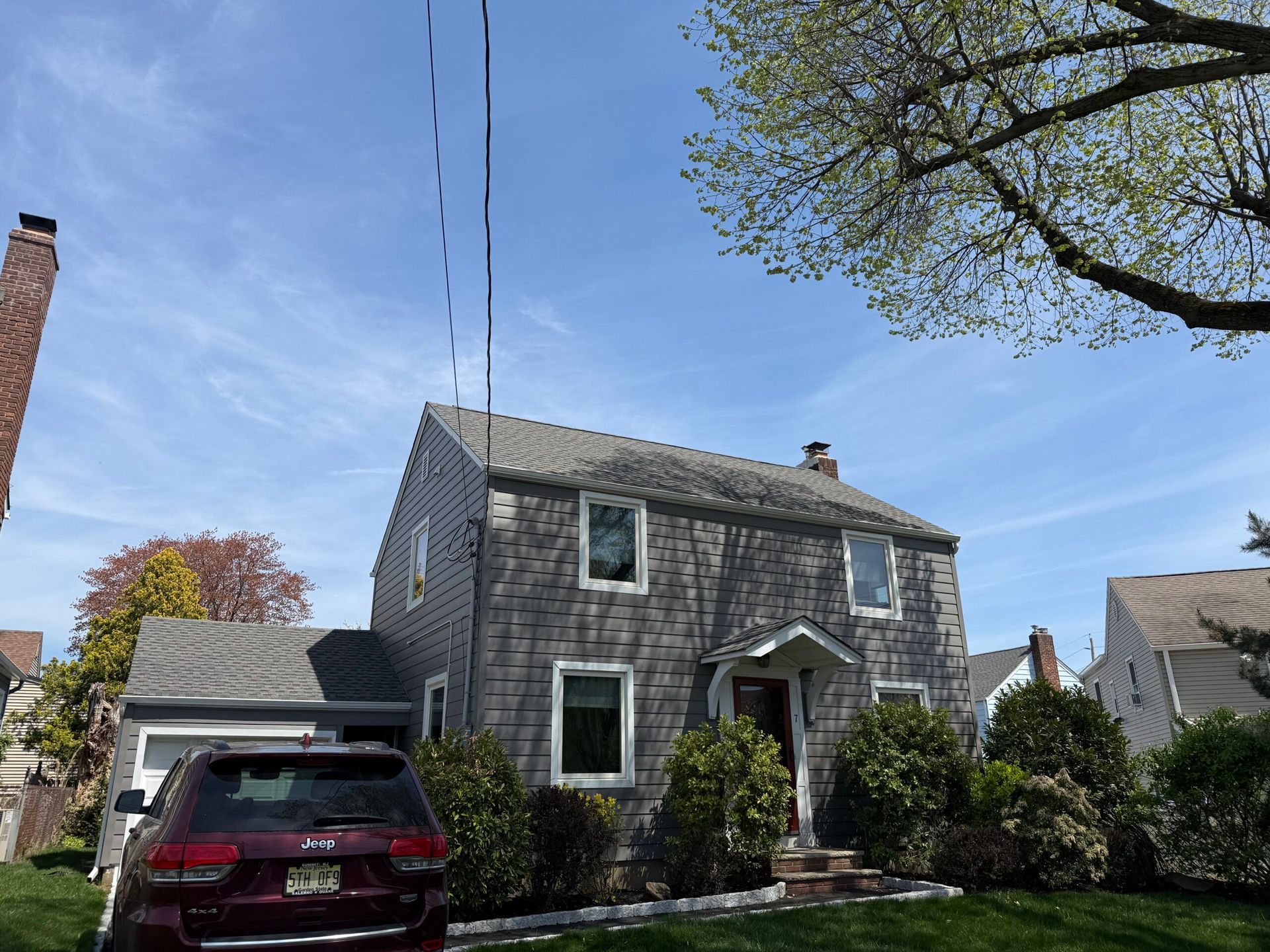 Stone house with a red SUV in the driveway under a blue sky, viewed from the street.