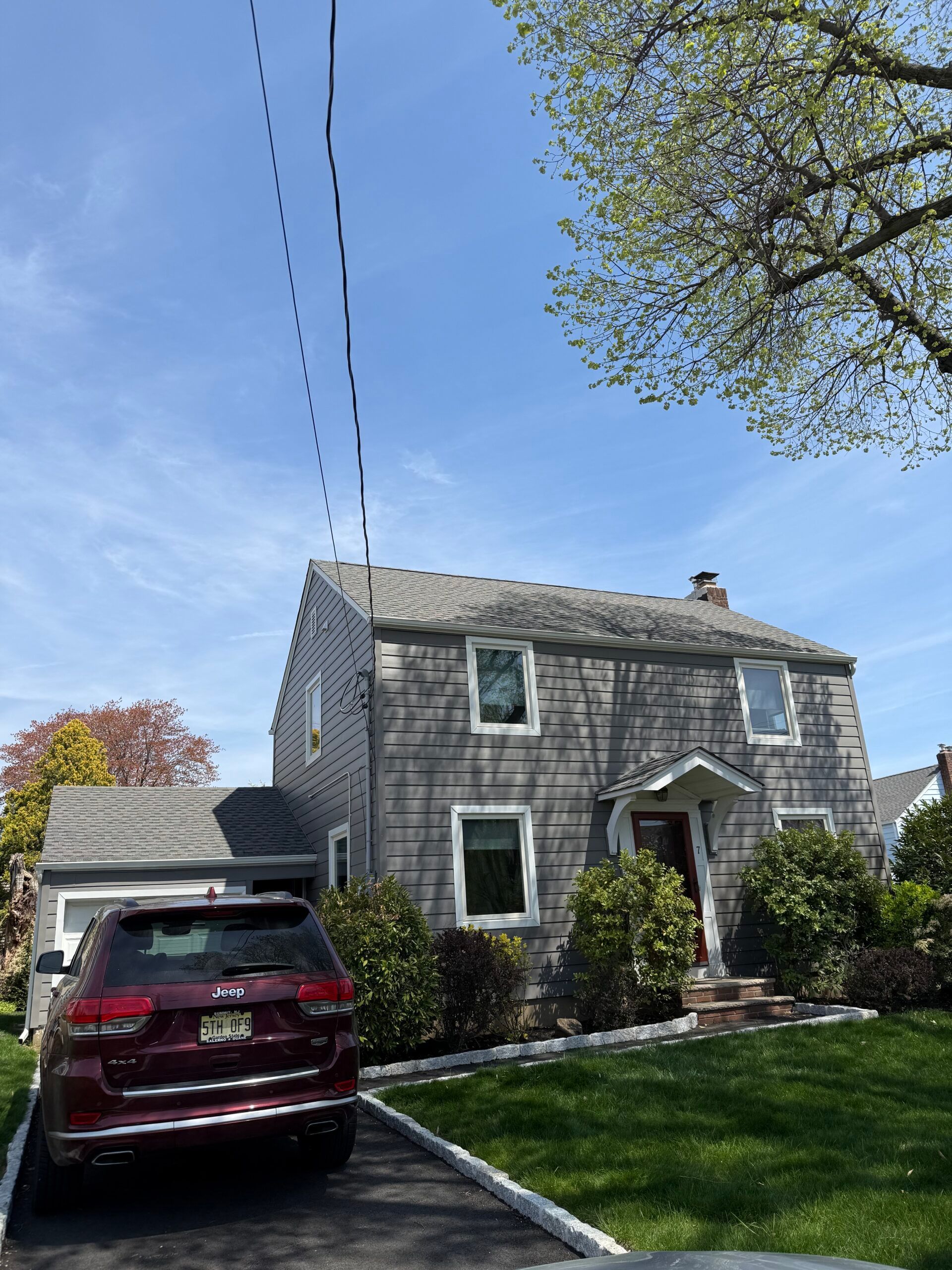 Suburban house with gray siding, red SUV in driveway, and green lawn under a blue sky