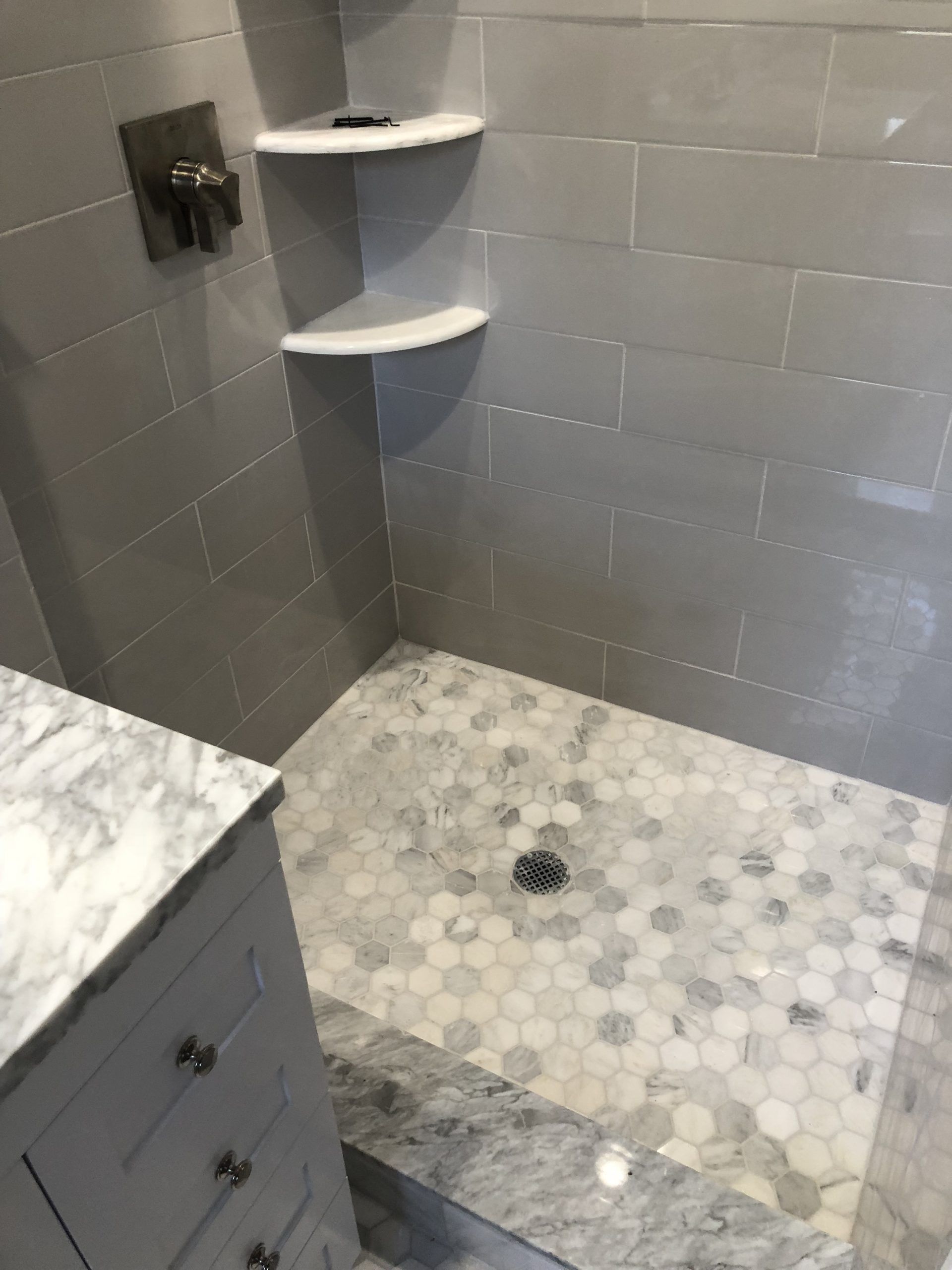 Tiled bathroom shower corner with pebble floor, glass shelf, and marble vanity edge
