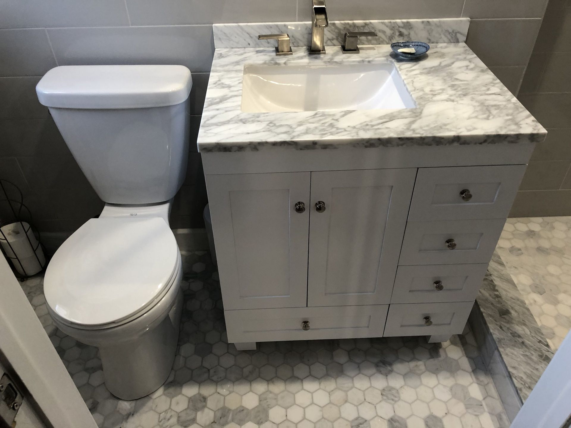White bathroom vanity with sink beside a toilet and gray tiled floor