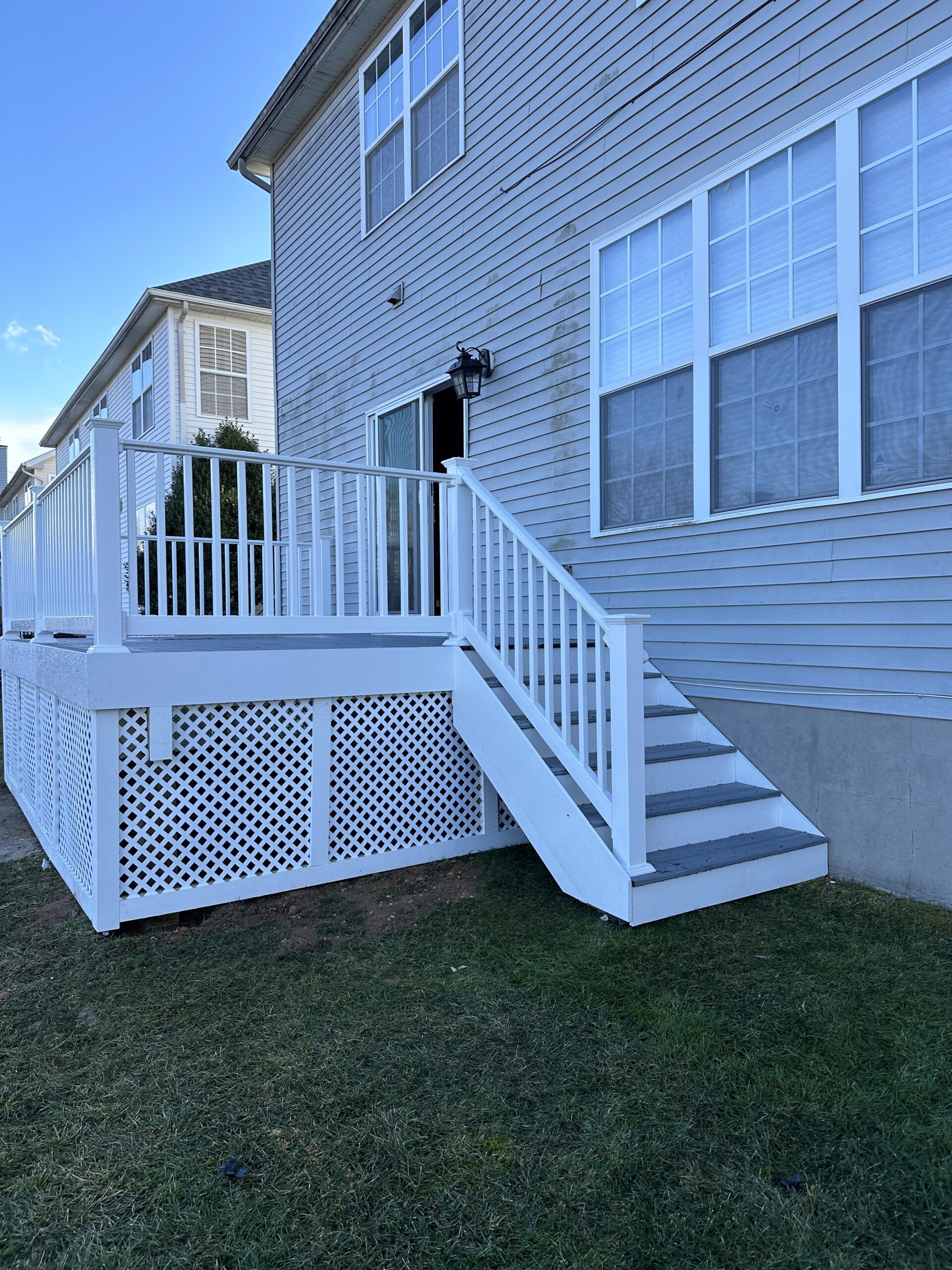 White house exterior with a raised deck, stairs, and lattice skirting under bright blue sky