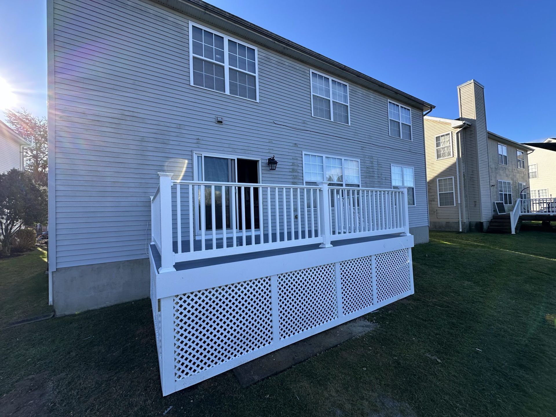 Back deck with white railing and lattice skirt on a gray house in a grassy yard