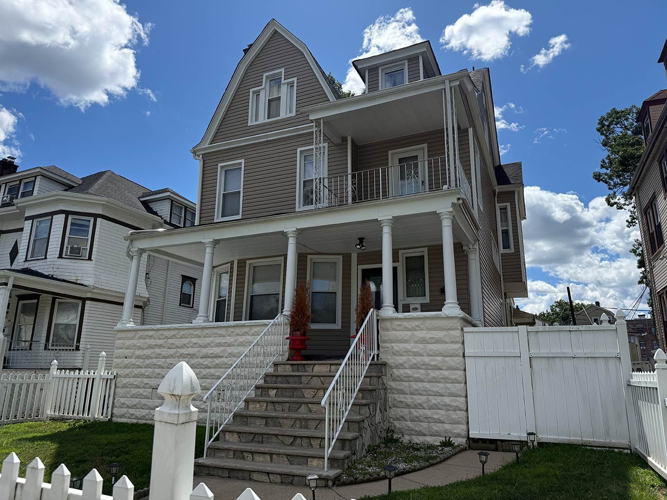 Victorian house with gray siding, white trim, red carpeted front steps, and a white picket fence under a blue sky